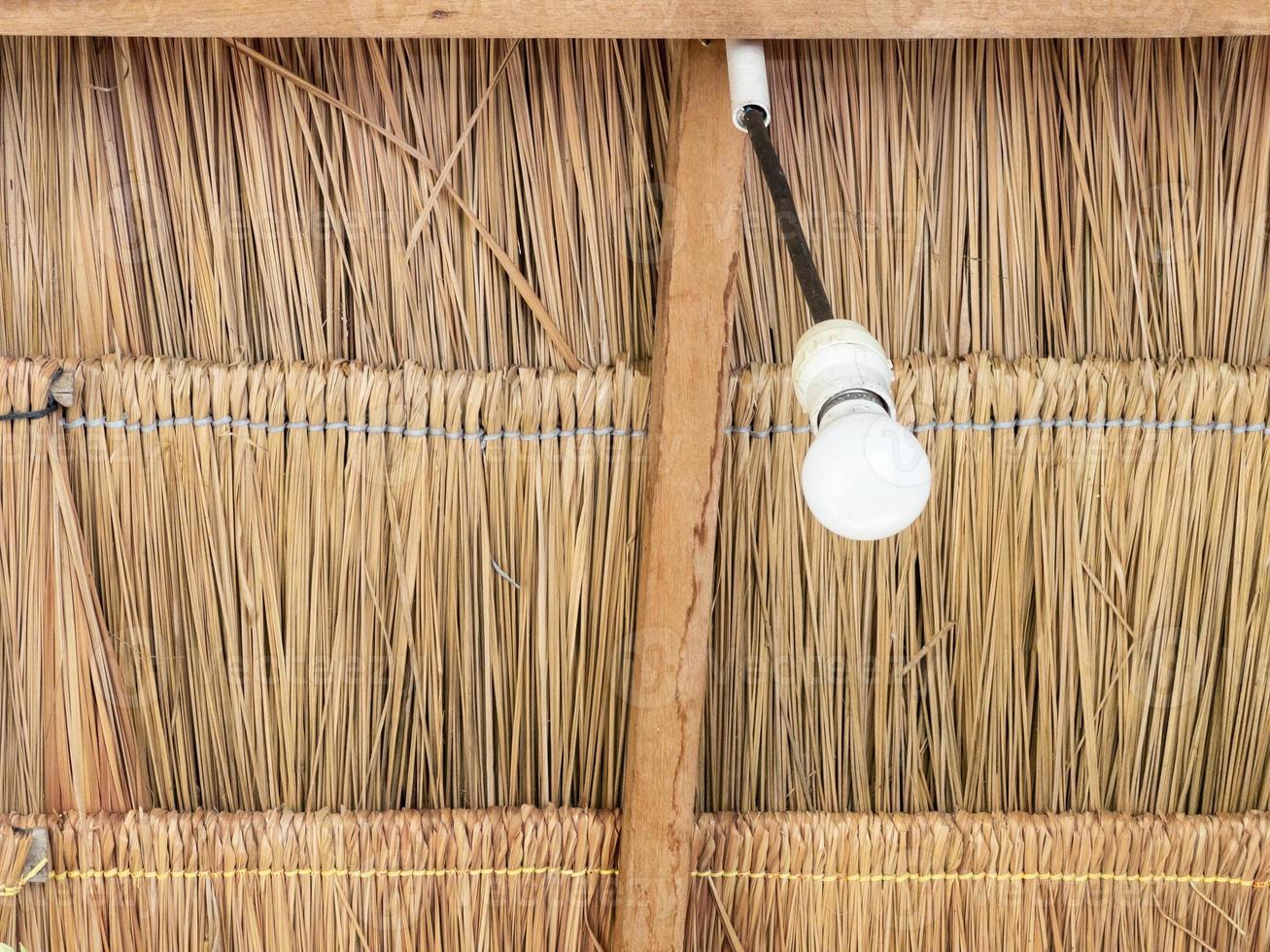 The LED bulb is hanging from the ceiling of the thatch. photo