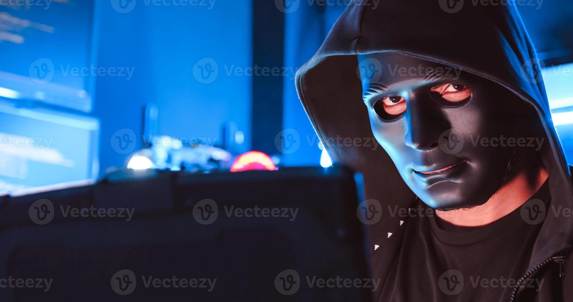 A hacker wearing a mask to cover his face is using computer to hack data to get ransom from victims. photo