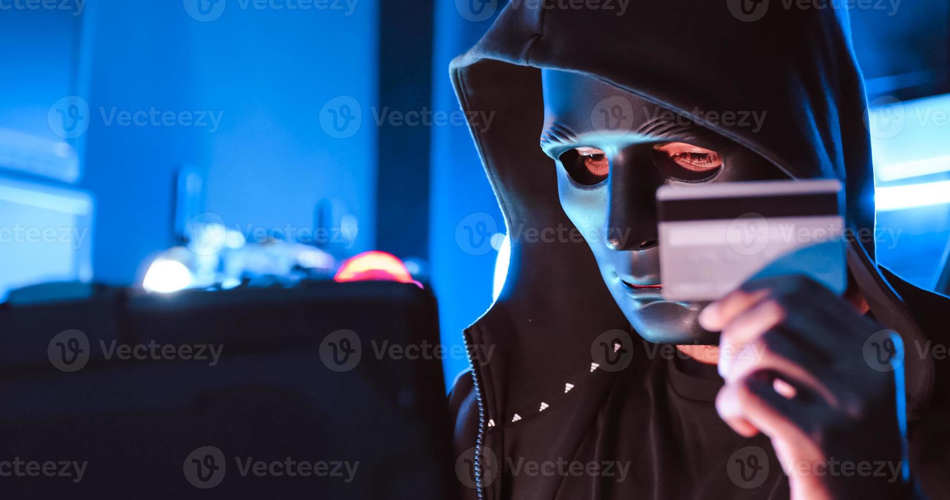 A hacker wearing a mask to cover his face is using computer to hack data to get ransom from victims. photo
