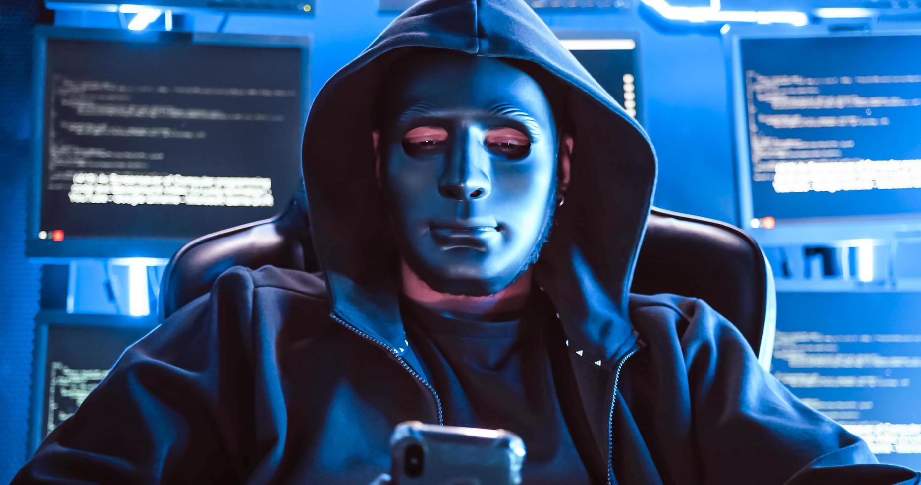A hacker wearing a mask to cover his face is using computer to hack data to get ransom from victims. photo