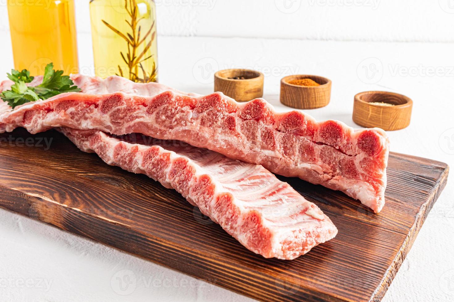 front view of juicy raw pork ribs on a cutting board. white background. spices for grilling ribs. photo