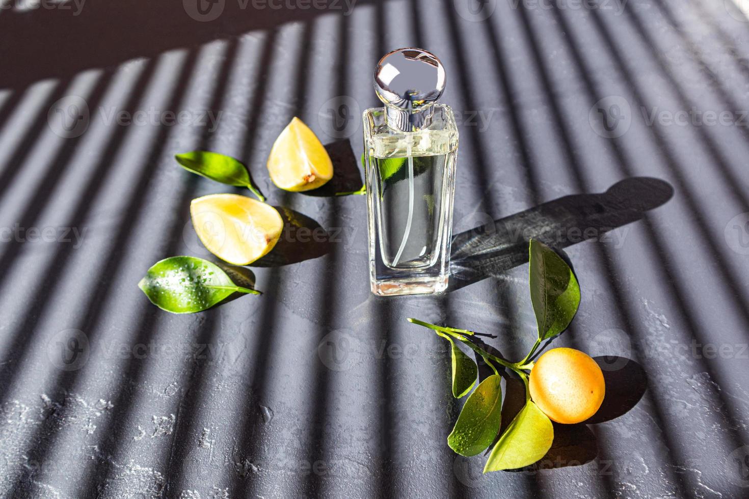 una botella transparente de cosmético con un aroma cítrico natural se encuentra sobre una mesa oscura con sombras paralelas desde las persianas de la ventana. foto