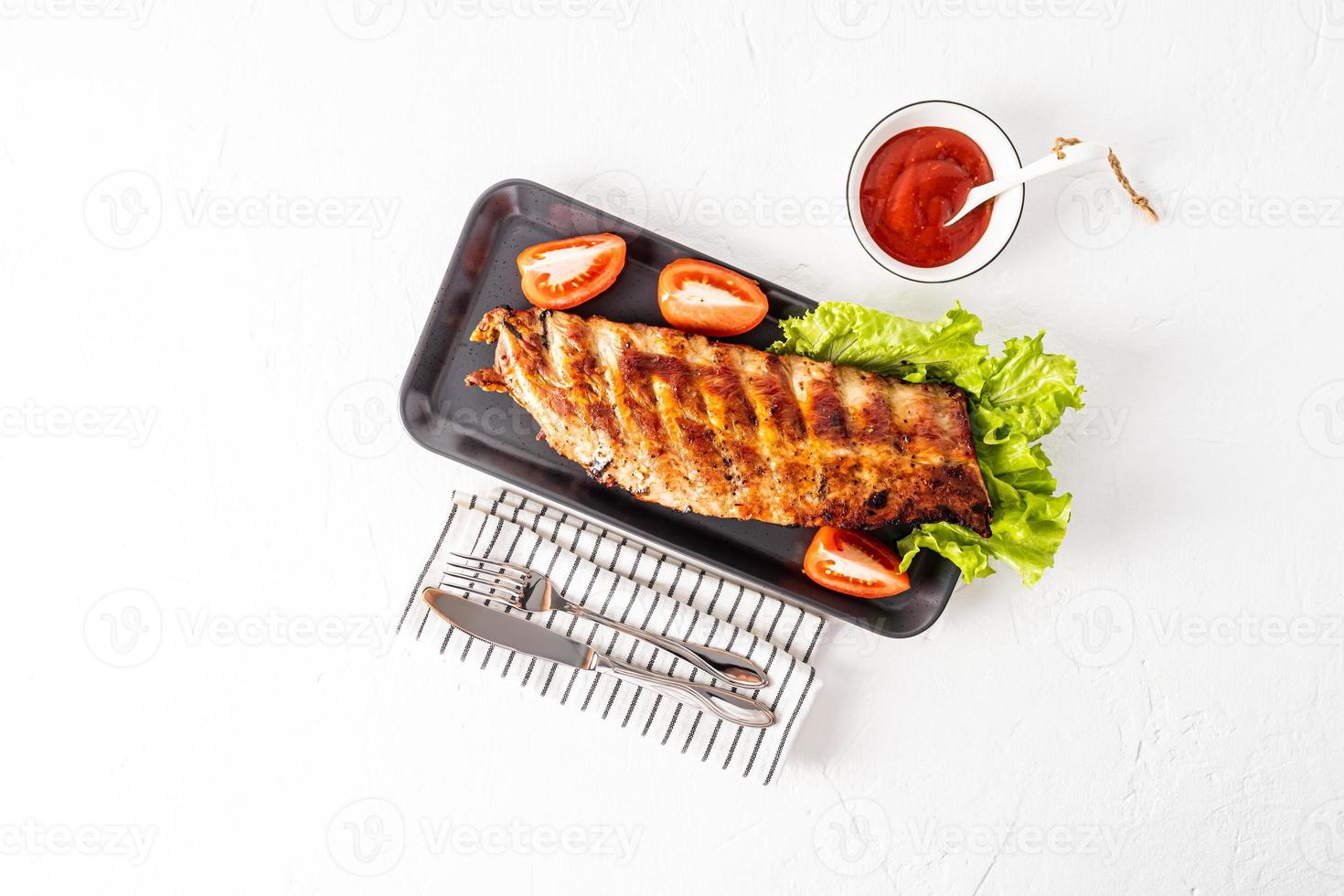 Top view of the delicious, juicy ribs of the barbecue on a ceramic tray with fresh vegetables. grilled pork ribs. sauce in a bowl . space for text. photo