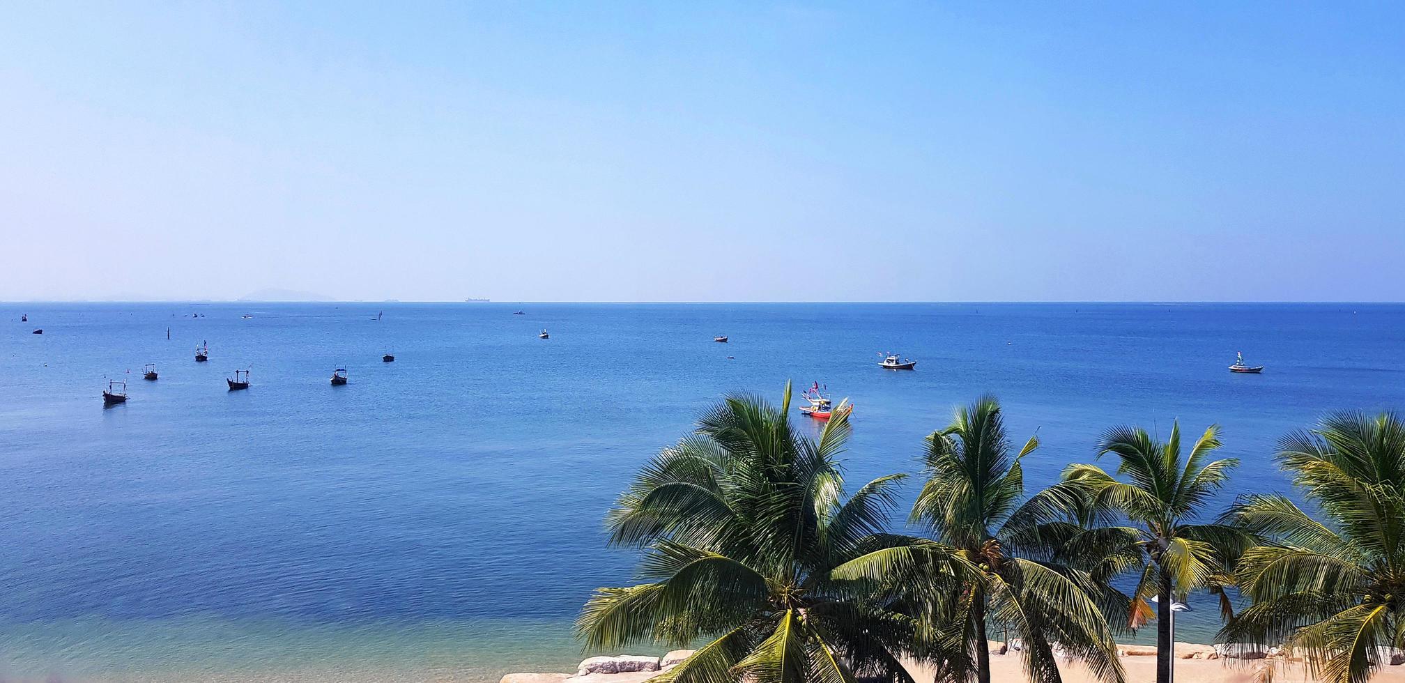 vista panorámica del mar con muchos barcos de pesca o de cola larga en el mar y cocoteros con fondo de cielo azul claro en chonburi, tailandia. belleza del papel tapiz natural en la playa con espacio para copiar. foto