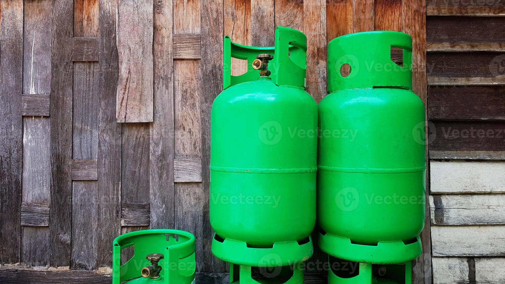 Green gas tanks on wooden wall or wallpaper with copy space on left. Group of object to make fire for cooking food in kitchen. Energy or Dangerous equipment keep away from heat or open flame and fire. photo