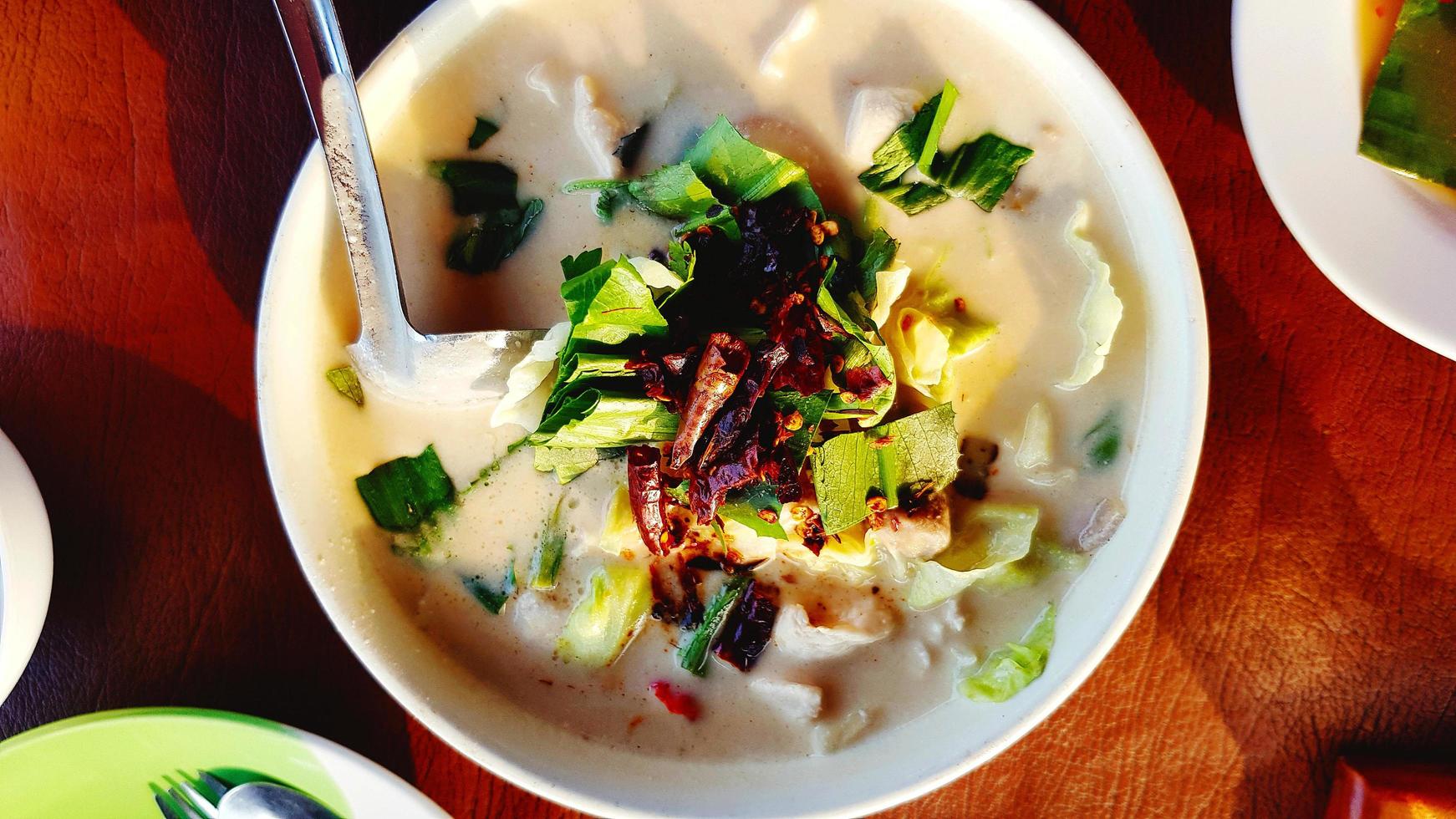 Flat lay of Thai spicy curry soup with chicken, coconut milk and herb Galangal, Lemongrass, kaffir lime leaves and dry red chili topping on top. This food called Tom Kha Gai from Thailand and famous photo