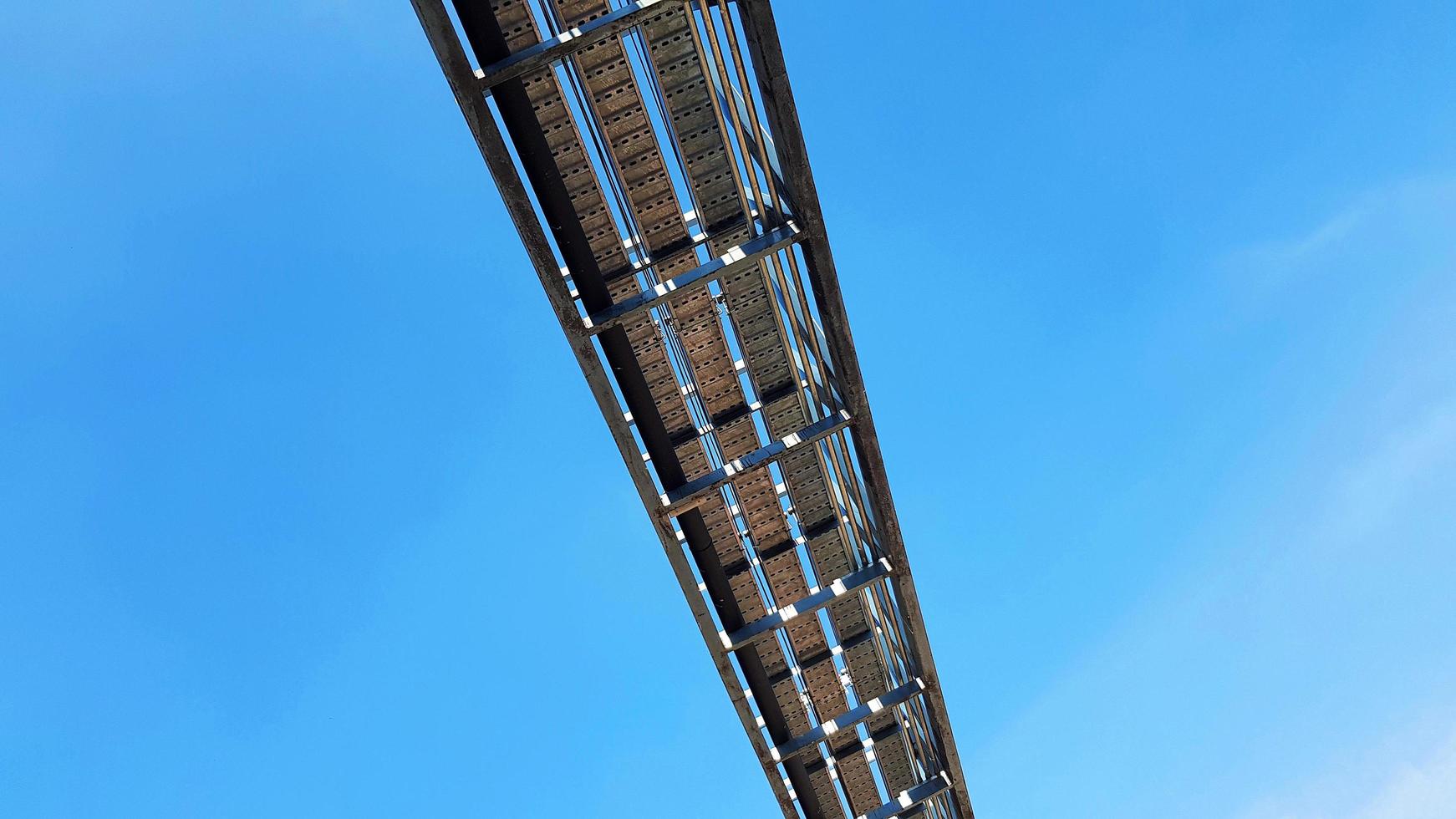 Bottom view of stainless steel electrical or communication cable tray with clear blue sky background with copy space. Iron bridge cross to air or heaven and industrial and installed system concept. photo