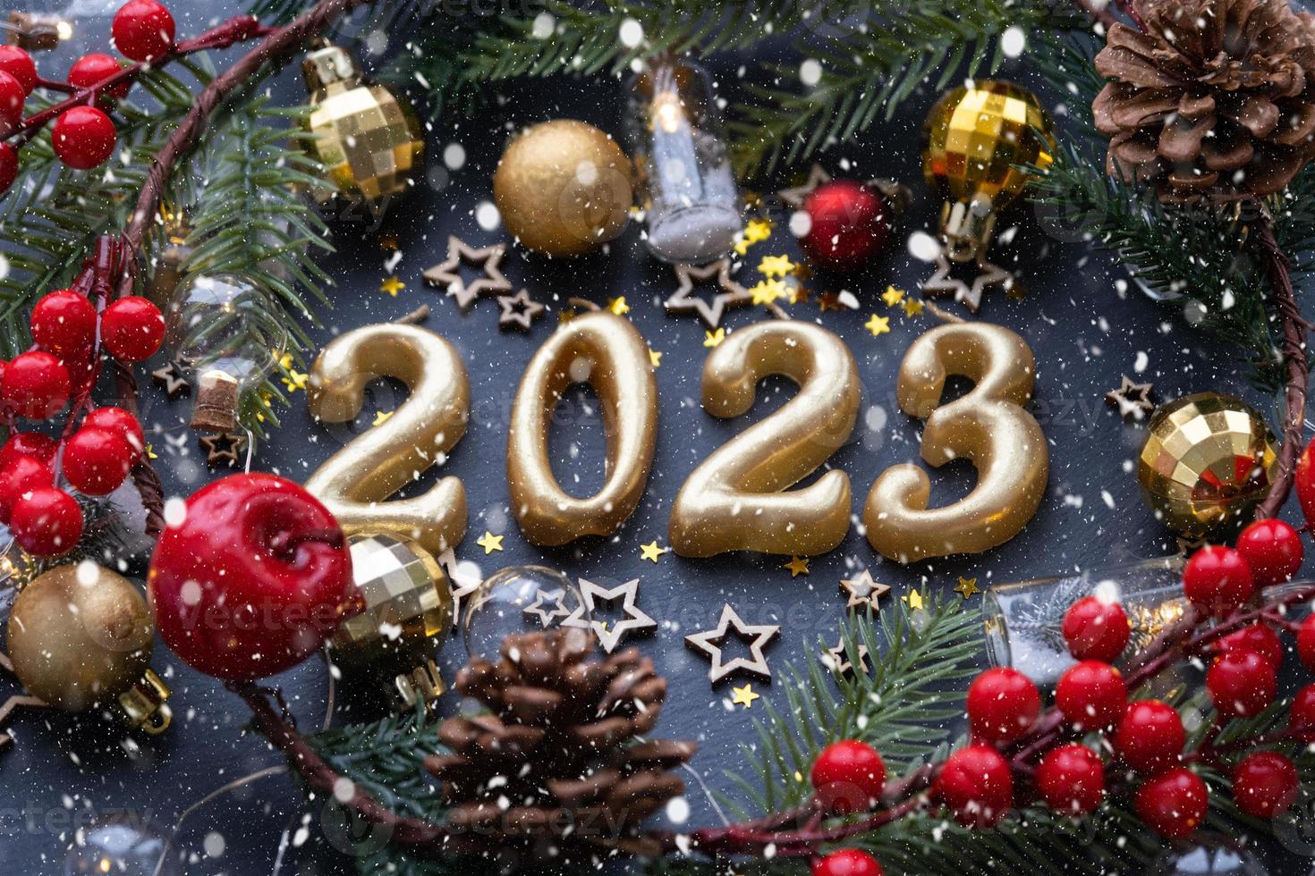 The golden figures 2023 made of candles on a black stone slate background are decorated with a festive decor of stars, sequins, fir branches, balls and garlands. Greeting card, happy New Year. photo