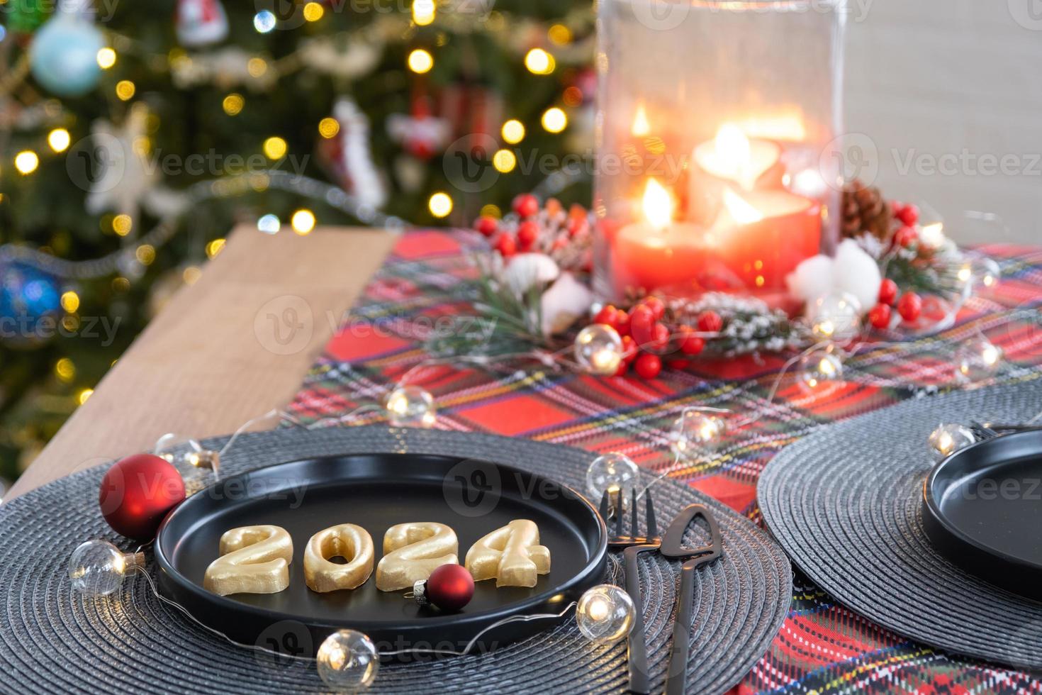 Golden figures 2024 from candles on a black plate on a festive table with a New Year's serving. Loft-style interior, party, feast. Wicker napkin, fork, knife photo