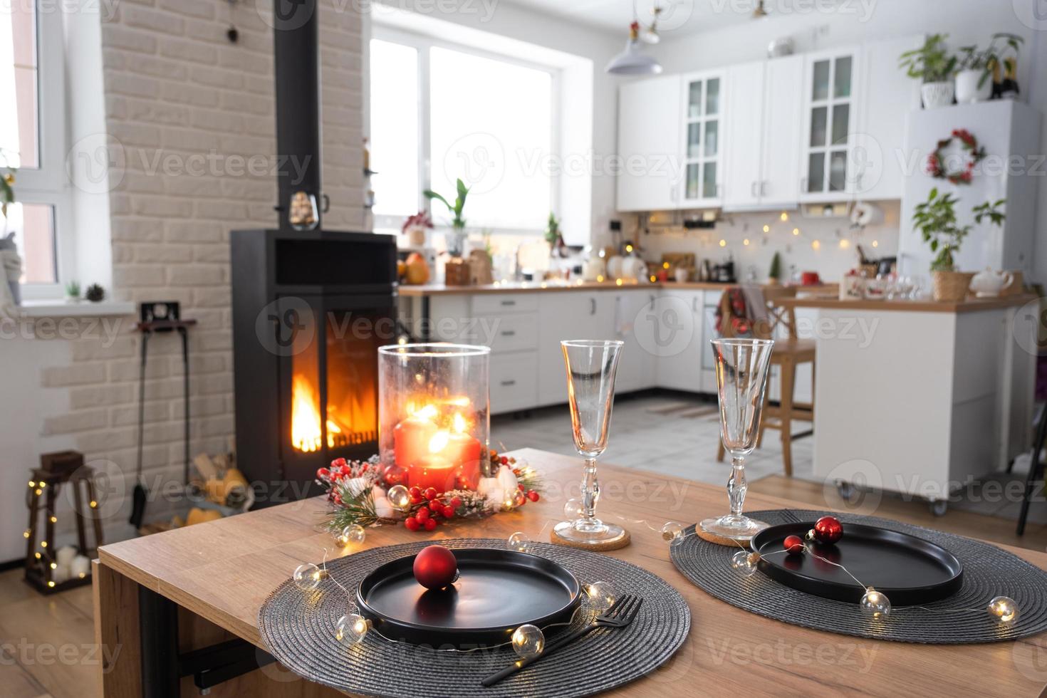 Festive interior of house is decorated for Christmas and New Year in loft style with black stove, fireplace, Christmas tree. Warm studio room with set table, burning wood, cozy and heating of home photo