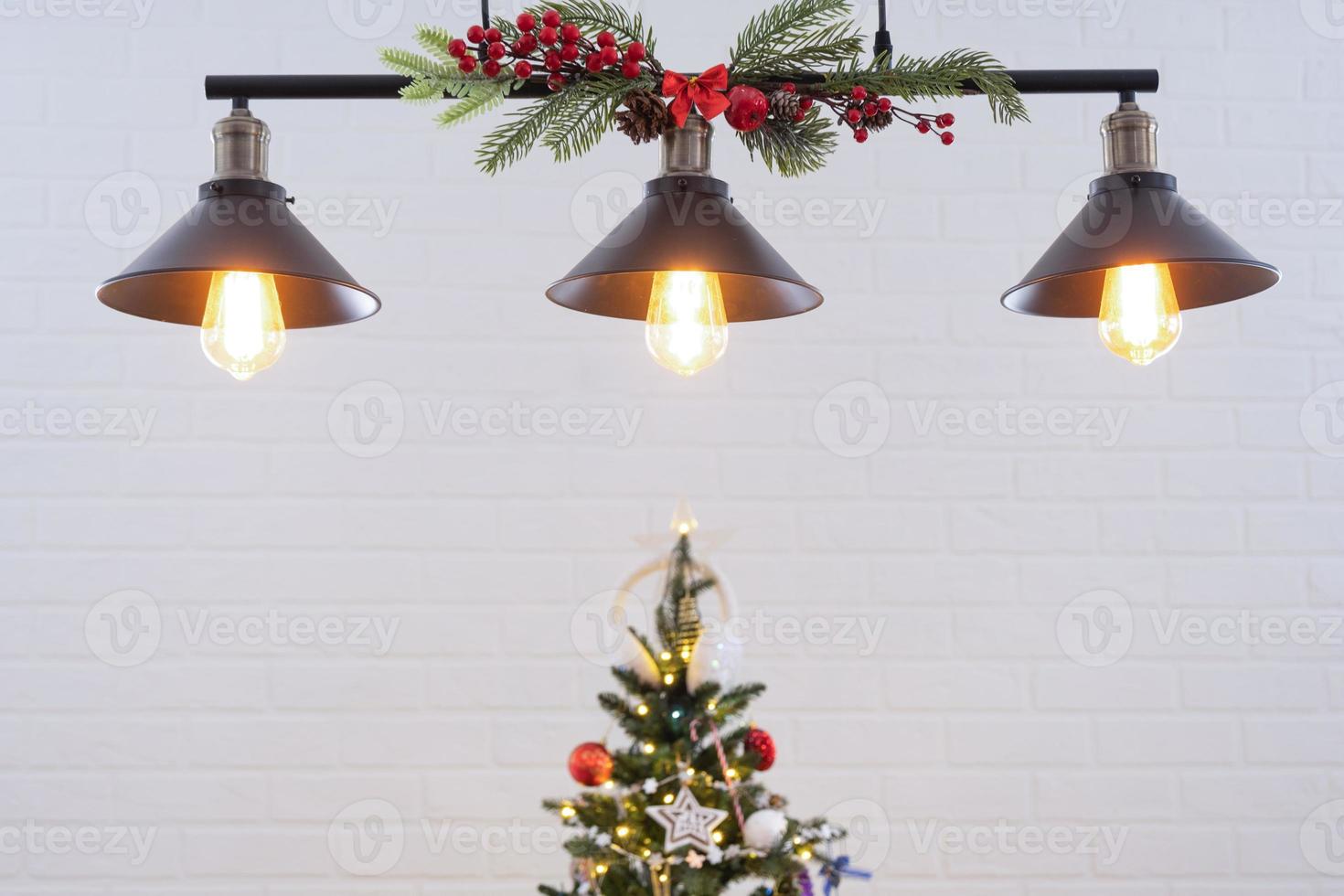 The black lampshade in the industrial loft style is decorated with spruce branches for Christmas and New Year on the background white brick wall. Close-up, minimalism photo