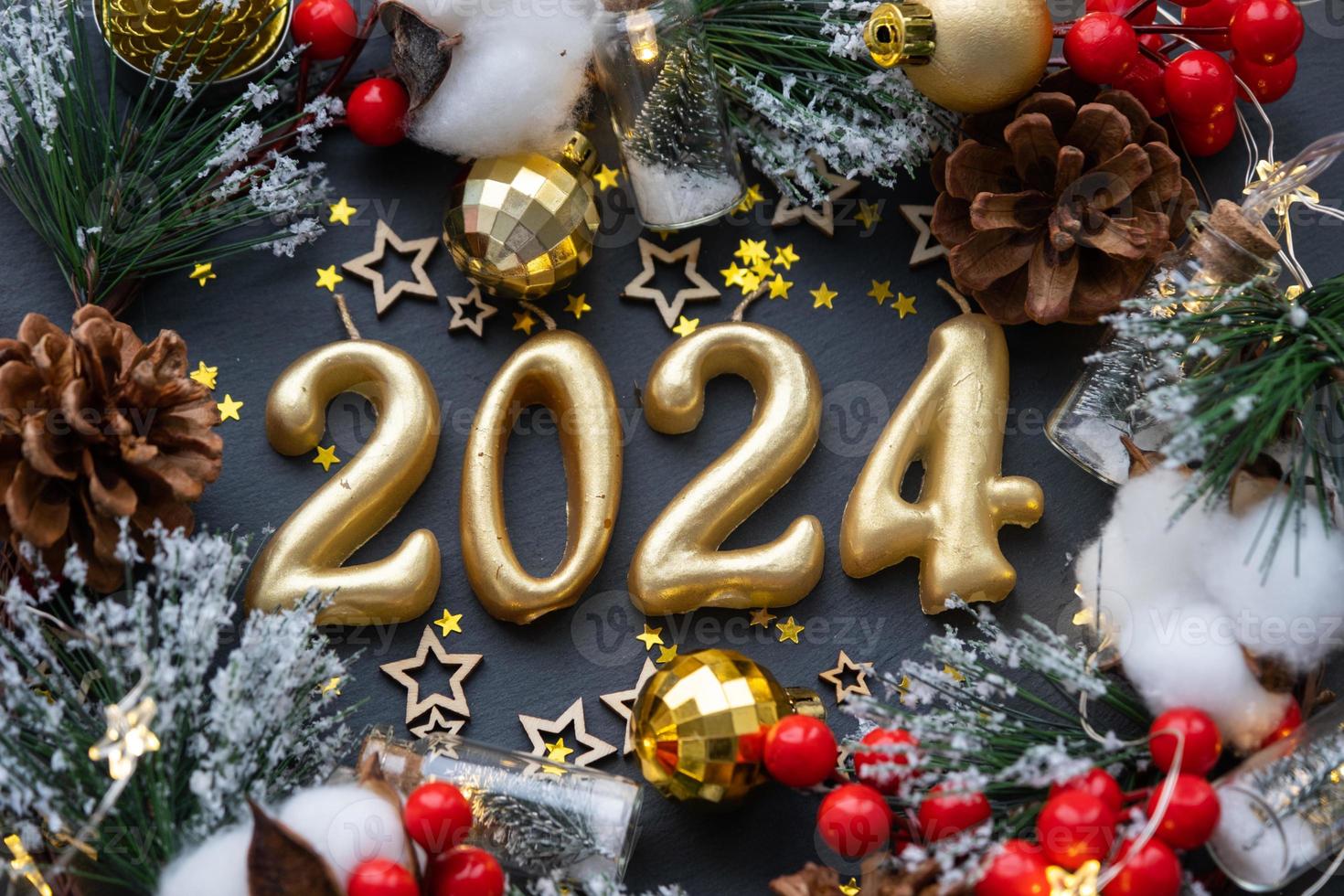The golden figures 2024 made of candles on a black stone slate background are decorated with a festive decor of stars, sequins, fir branches, balls and garlands. Greeting card, happy New Year. photo