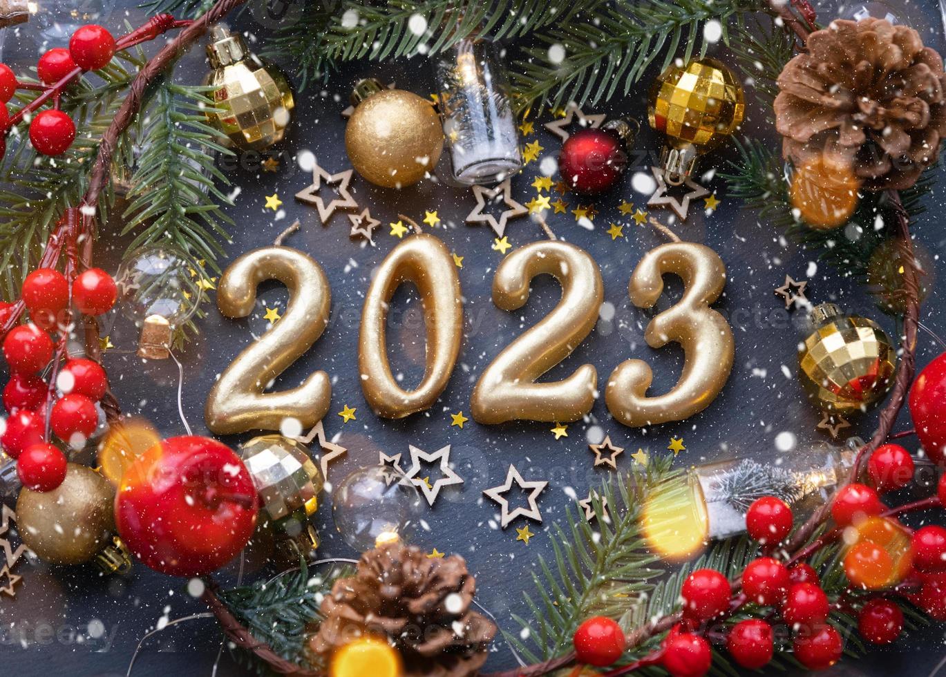 las figuras doradas 2023 hechas de velas sobre un fondo de pizarra de piedra negra están decoradas con una decoración festiva de estrellas, lentejuelas, ramas de abeto, bolas y guirnaldas. tarjeta de felicitación, feliz año nuevo. foto