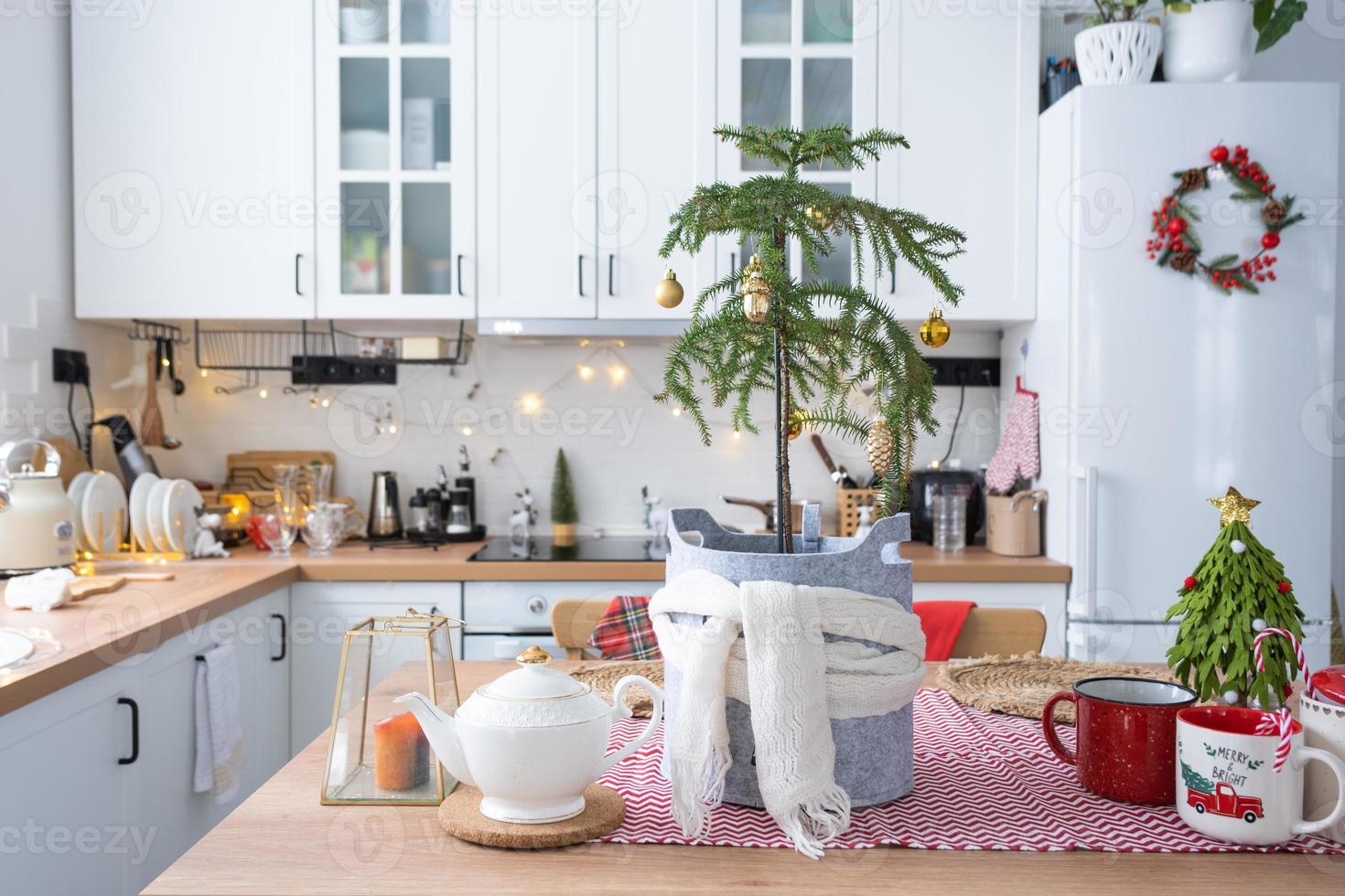 decoración navideña festiva en cocina blanca, desayuno festivo, interior escandinavo blanco. Se decora araucaria como árbol de navidad y se envuelve en una bufanda y maceteros de fieltro. año nuevo, estado de ánimo, hogar acogedor foto