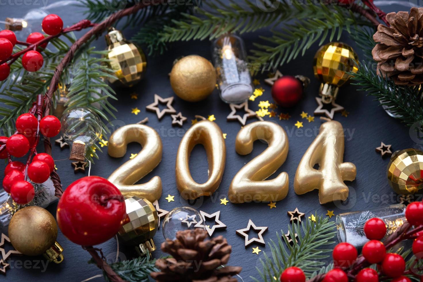 The golden figures 2024 made of candles on a black stone slate background are decorated with a festive decor of stars, sequins, fir branches, balls and garlands. Greeting card, happy New Year. photo