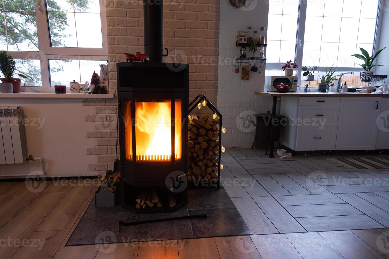 Black metal stove fireplace with wood in a woodpile - the interior of a private village house. Heating and heating of the house with firewood, the heat of the fire from the hearth. photo