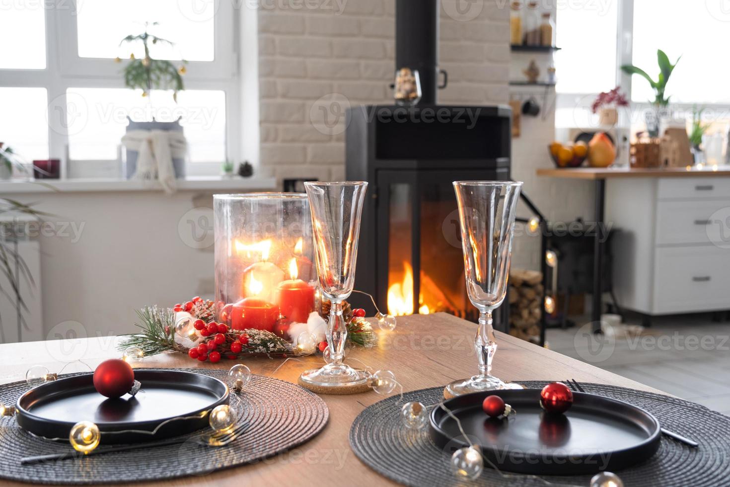 Festive interior of house is decorated for Christmas and New Year in loft style with black stove, fireplace, Christmas tree. Warm studio room with set table, burning wood, cozy and heating of home photo