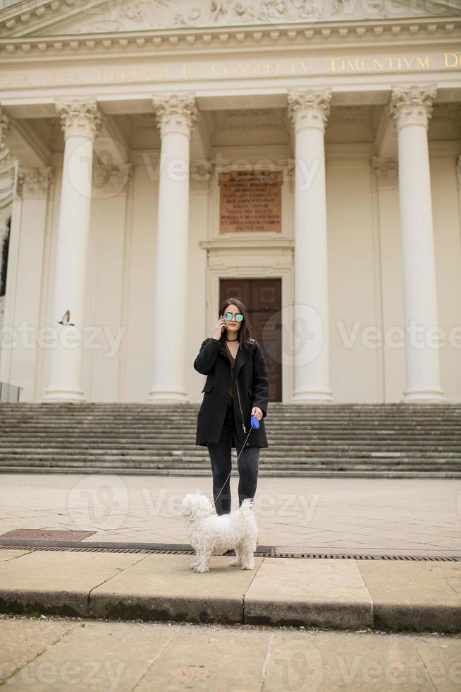 hermosa joven feliz con un lindo cachorro de perro pequeño usando un teléfono móvil en la calle foto