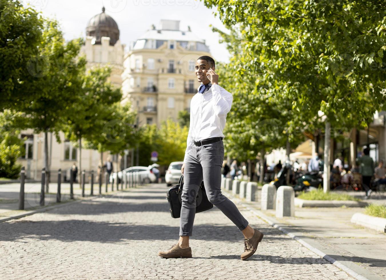 Young African American businessman using a mobile phone while crossing a street photo