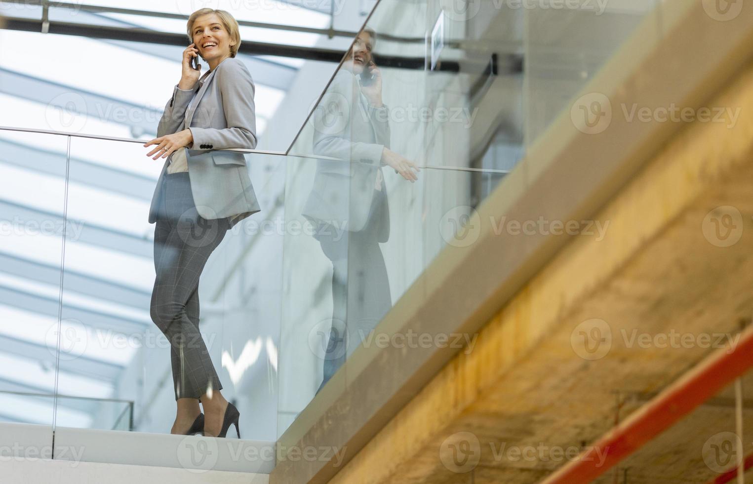 mujer de negocios que usa teléfono móvil en el pasillo de la oficina moderna foto