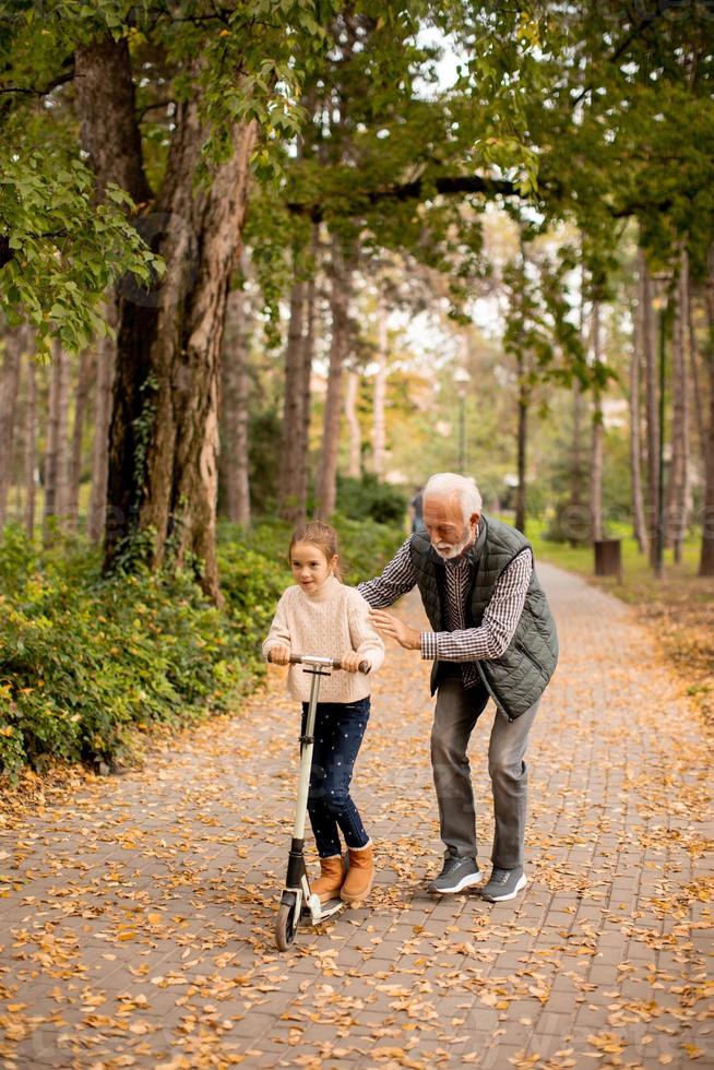 un anciano enseñando a su nieta a andar en patinete en el parque foto