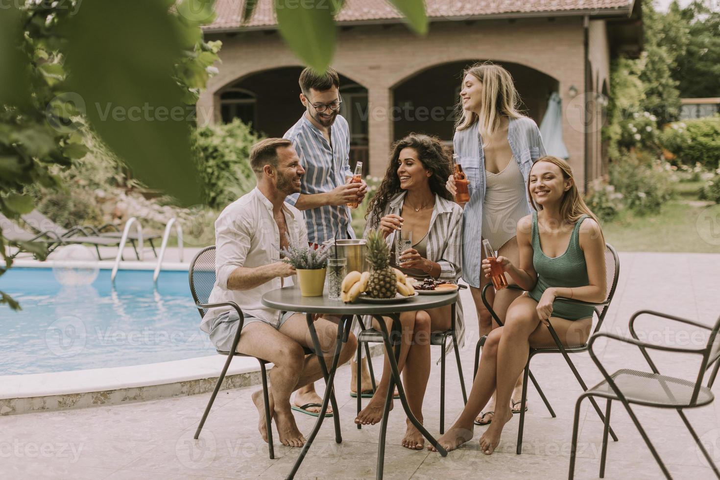 grupo de jóvenes animando con sidra junto a la piscina en el jardín foto