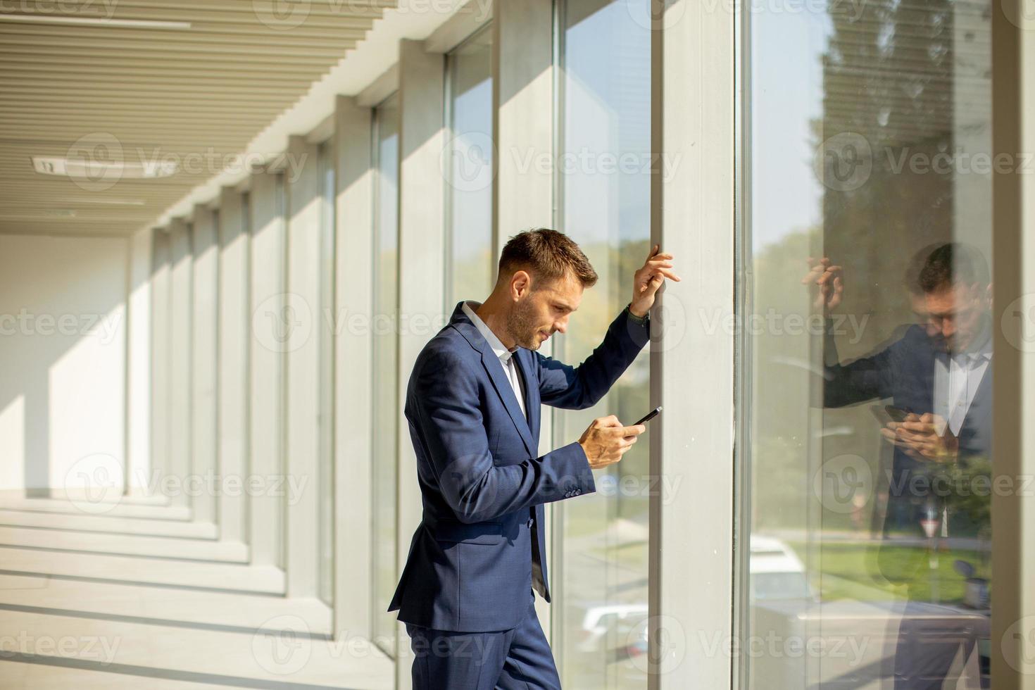 Young business man using mobile phone in the modern office hallway photo