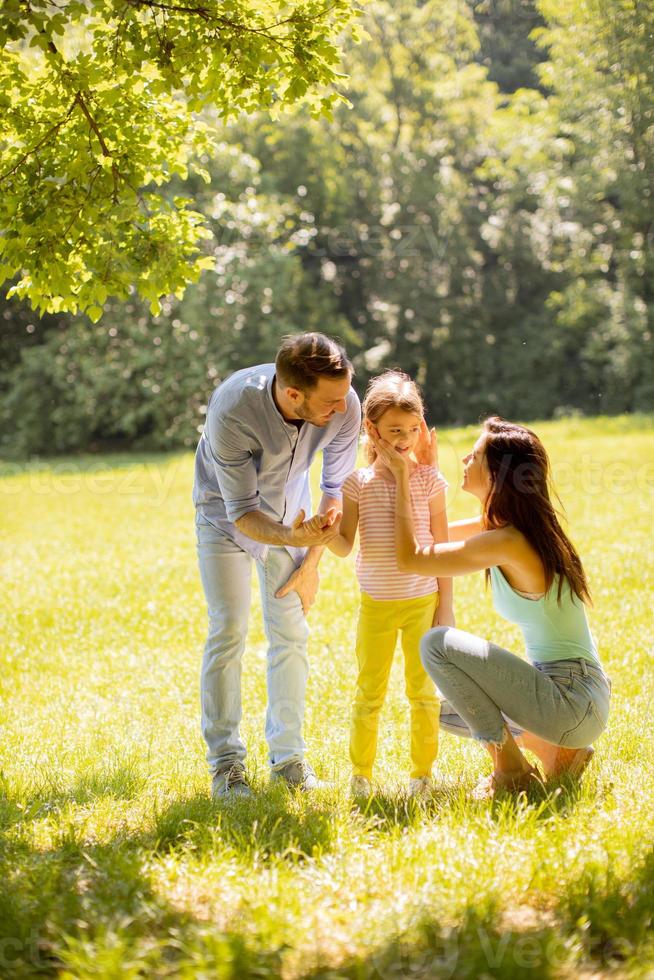 Familia joven feliz con linda hijita divirtiéndose en el parque en un día soleado foto