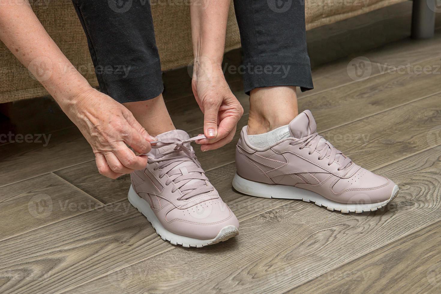 hands of an age woman put shoes on and tie shoelaces in sneakers photo