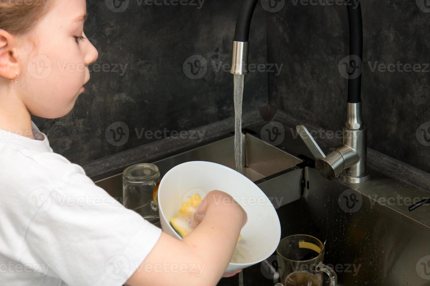 cute little girl washing dishes in the kitchen by the sink photo