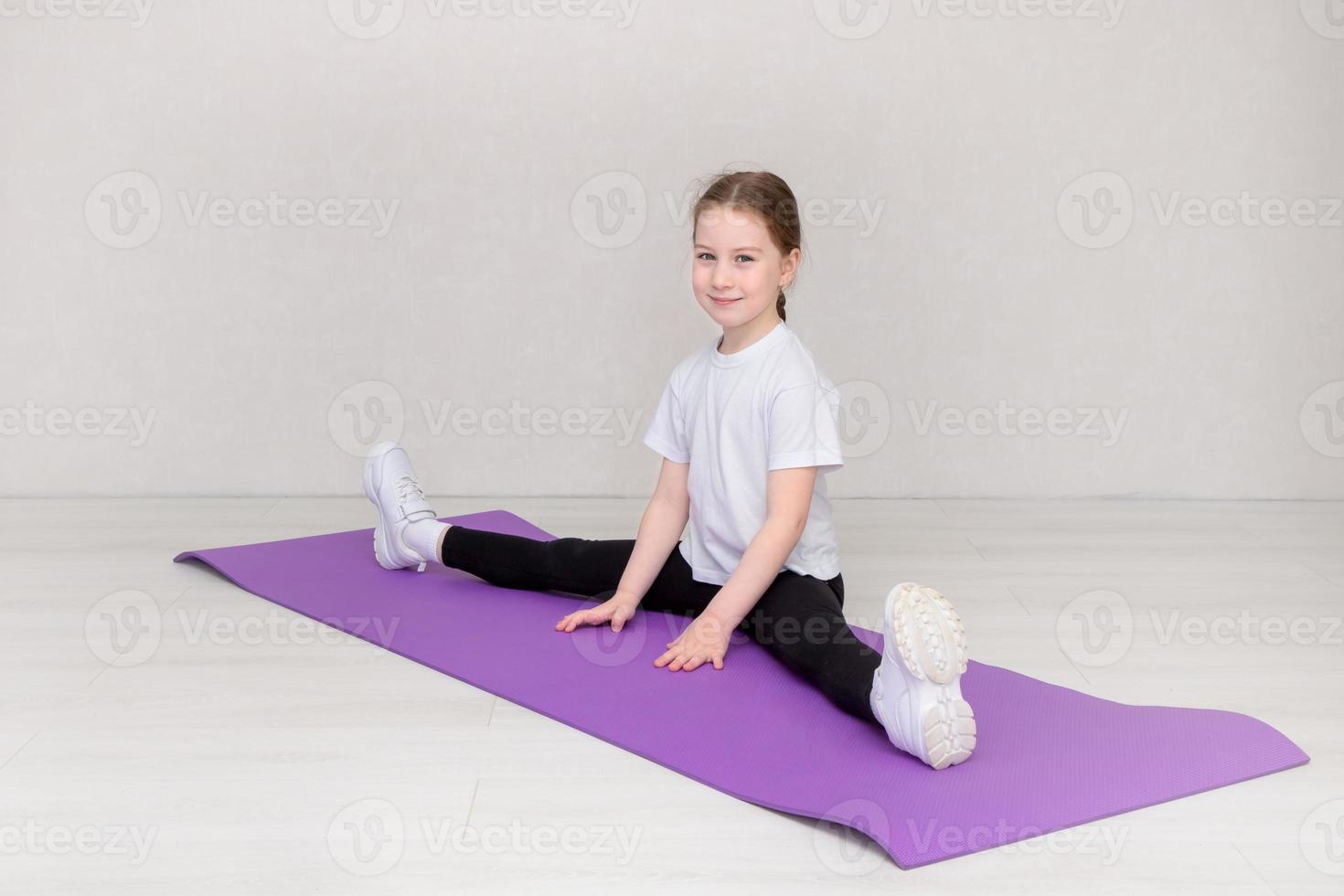 linda niña se sienta en una pierna dividida en una alfombra hymantic y sonríe foto
