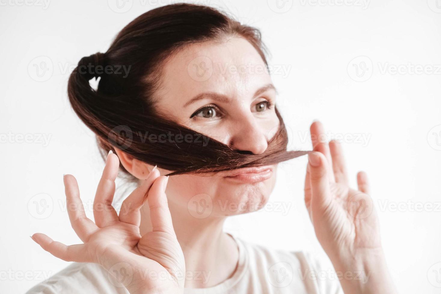 Portrait of a beautiful woman who makes a mustache out of pigtails and a funny face on a white background photo