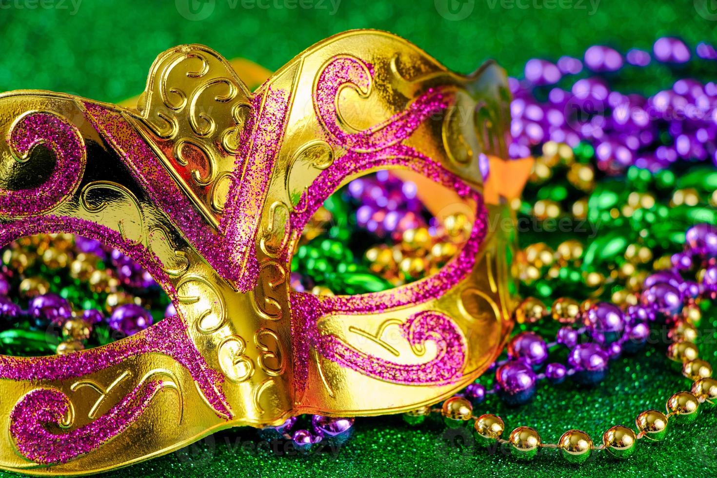 Carnival mask and colorful beads on green shiny background. Mardi Gras concept. Fat Tuesday symbol. photo