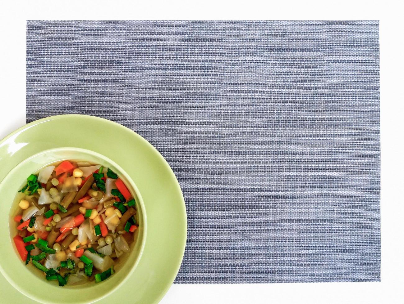 Simple vegetable soup in green bowl,  gray placemat, top view, copy space photo