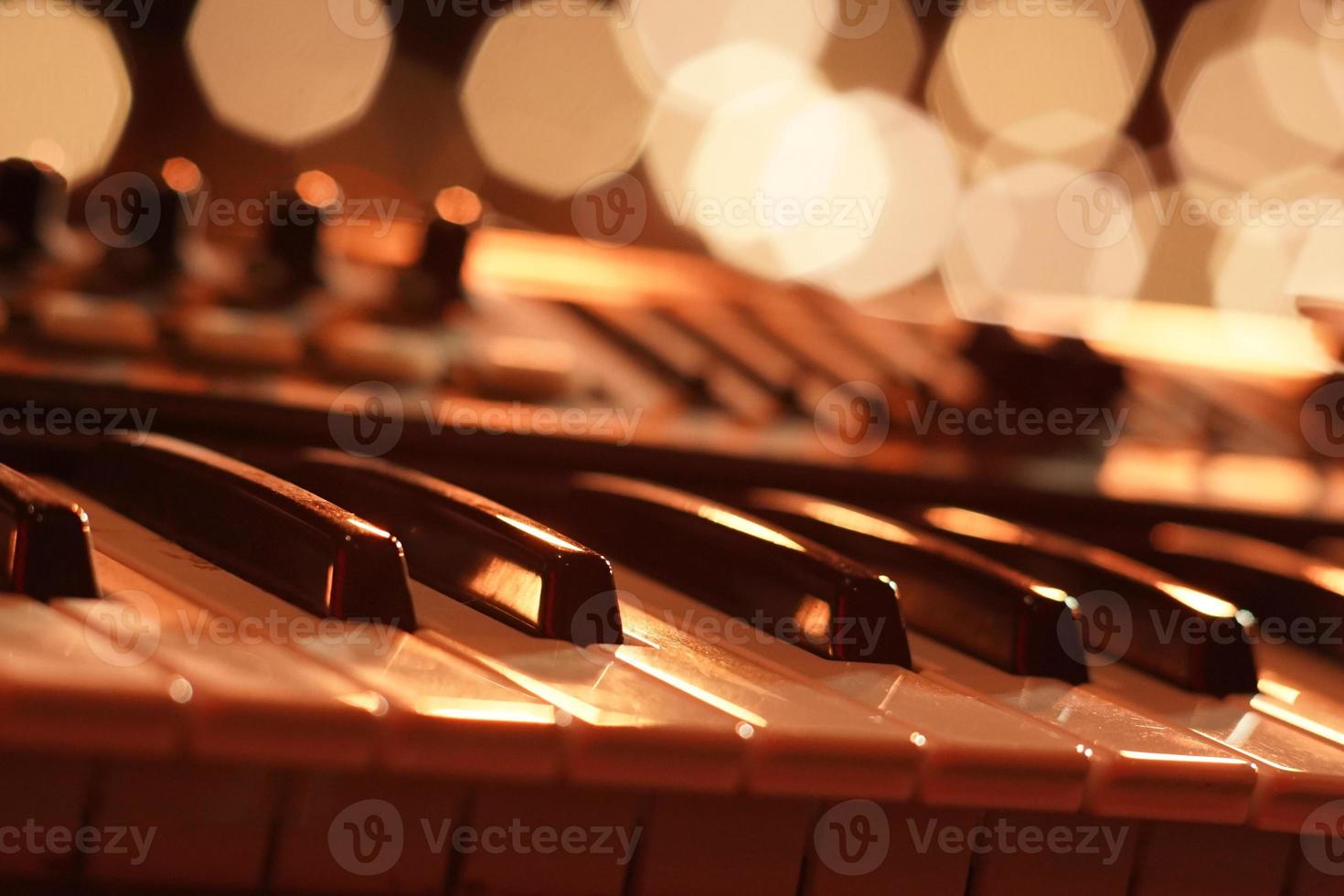 A piano is seen in a beautiful and romantic setting. The photo is a macro shot that captures the intricate details of the piano's keys and the golden bokeh of the background lights.