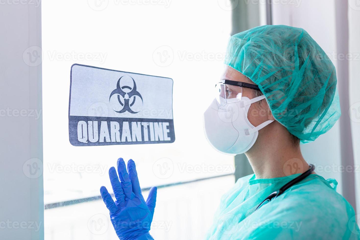 Worried female doctor looking through the hospital window, Quarantine alert sign in hospital with doctor, nurse with mask and protective suit. Corona virus outbreak photo