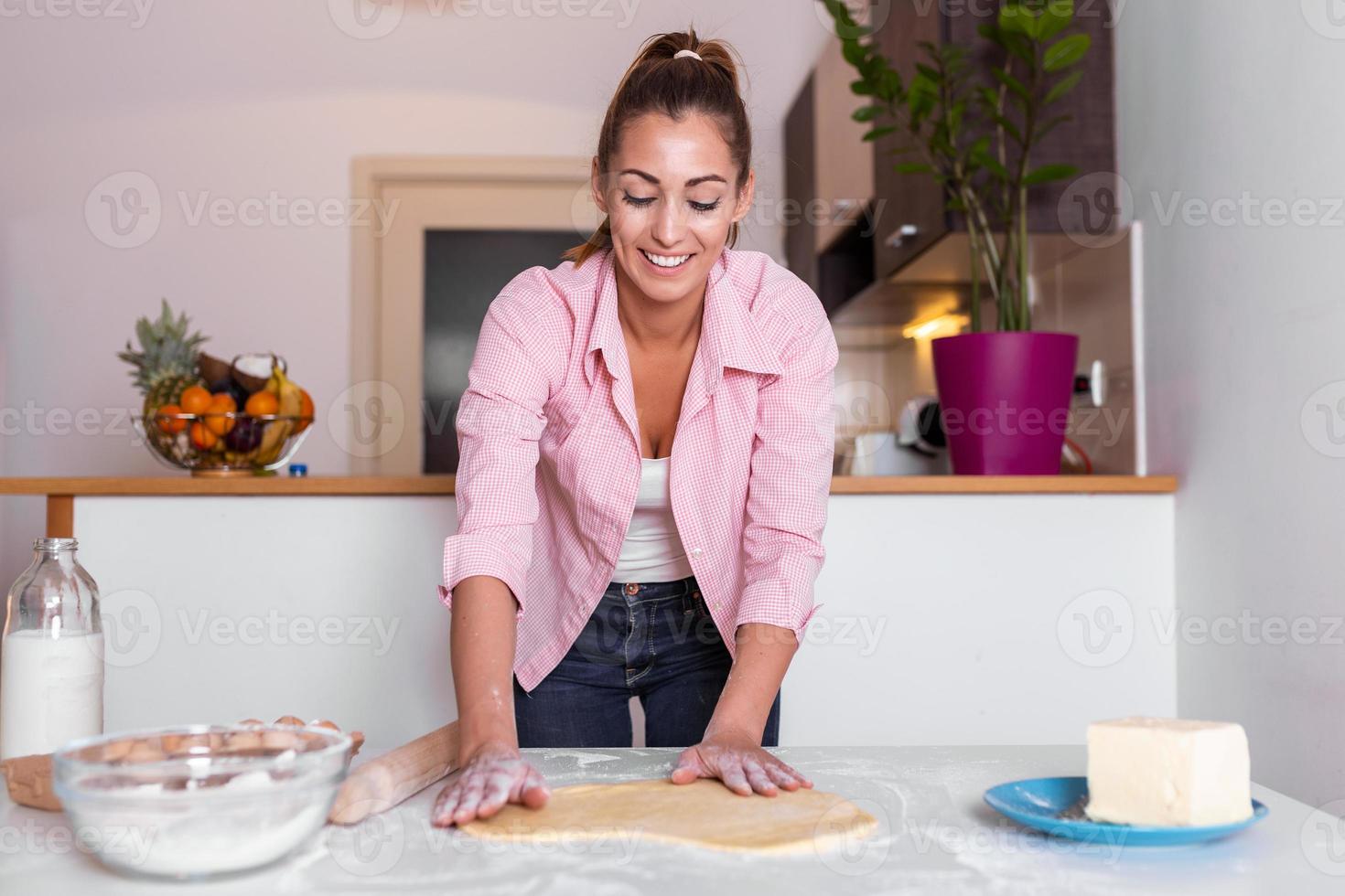 Beautiful young woman looking at camera and smiling while baking in kitchen at home. Smiling young housewife making dough photo