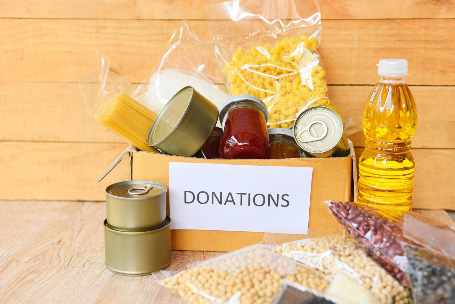 caja de donaciones con comida enlatada en el fondo de la mesa de madera pasta enlatada y alimentos secos no perecederos con aceite de cocina fideos de arroz espagueti macarrones donaciones concepto de comida foto