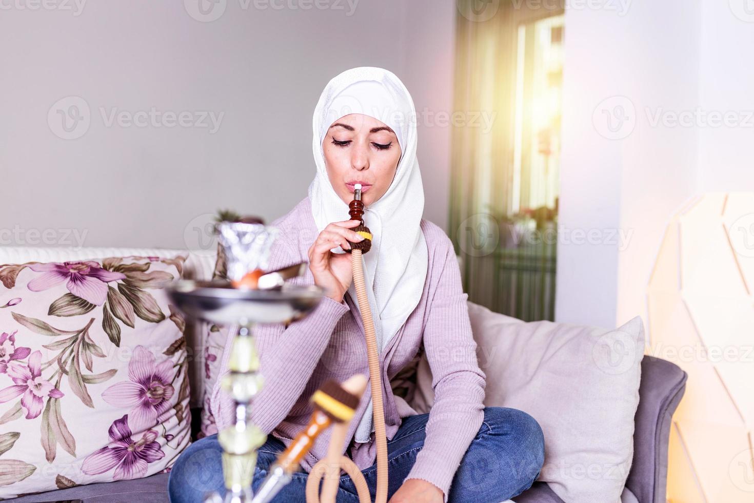 mujer musulmana fumando shisha en casa. joven musulmana disfrutando mientras fuma narguile. chica árabe fumando narguile foto