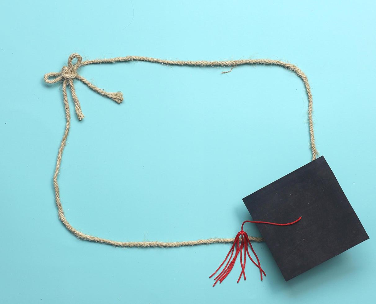 Education rope frame - Top view of rope frame tie as bow and graduated cap at the corner on light blue background photo