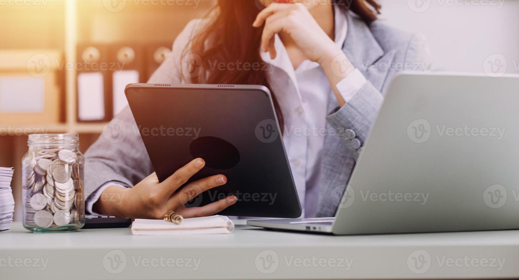 Young business woman sitting in office at table and using smartphone. On desk is laptop and tablet computer, on screen charts and graphs. Woman analyzing data. Student learning online. photo
