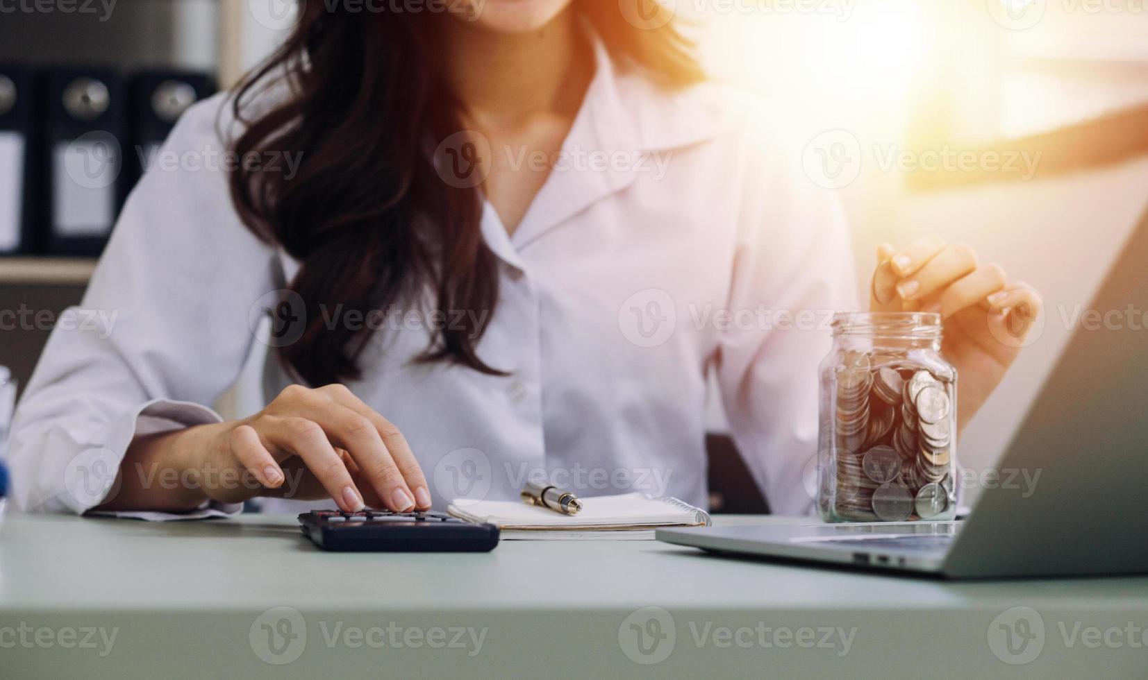 Young business woman sitting in office at table and using smartphone. On desk is laptop and tablet computer, on screen charts and graphs. Woman analyzing data. Student learning online. photo