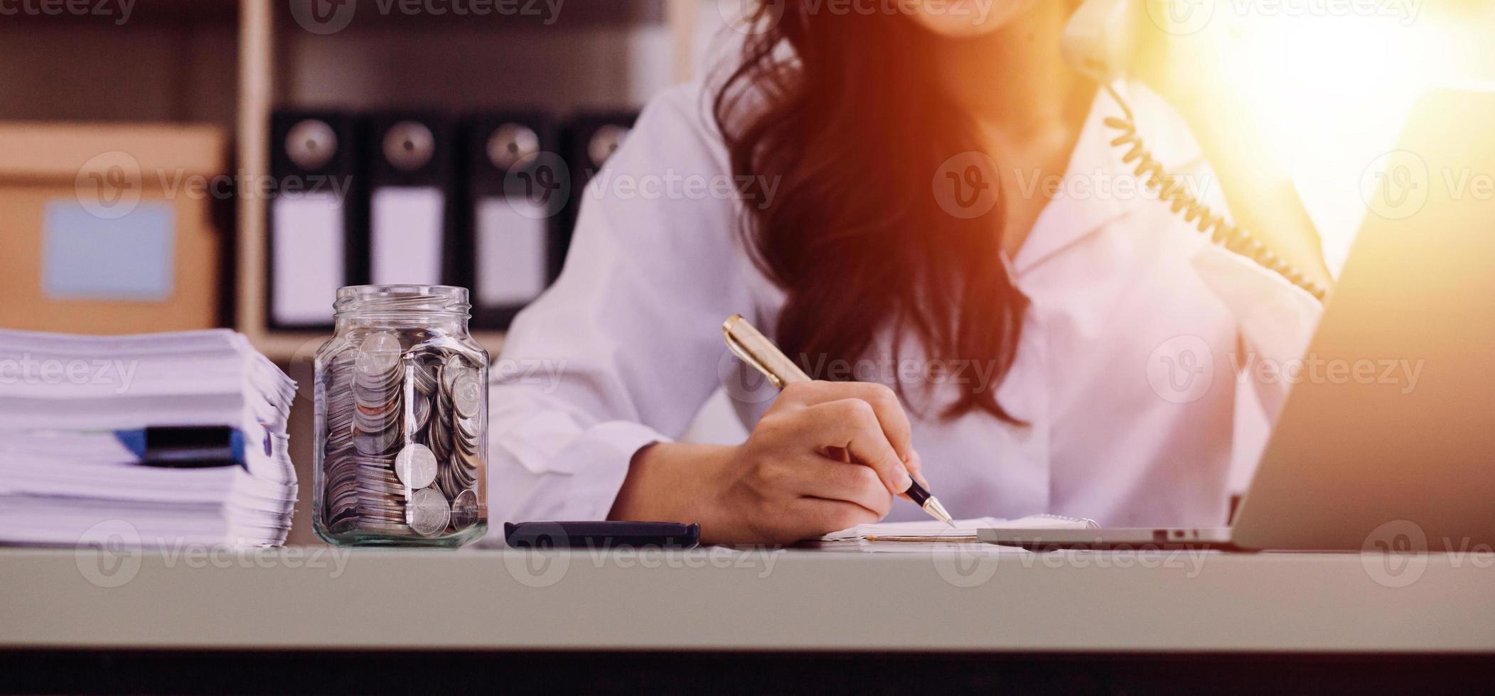 Young business woman sitting in office at table and using smartphone. On desk is laptop and tablet computer, on screen charts and graphs. Woman analyzing data. Student learning online. photo