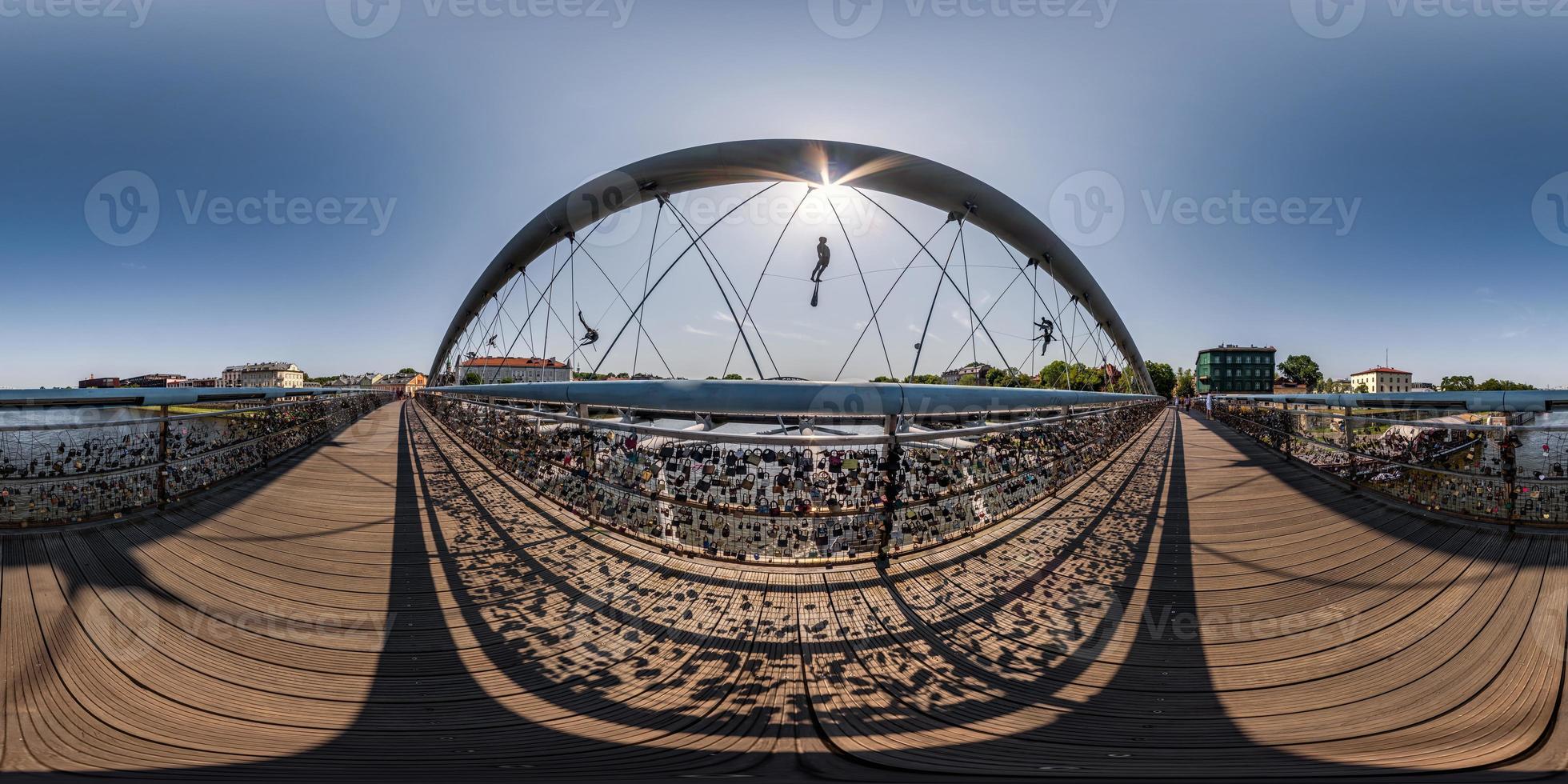 vista panorámica hdri 360 esférica completa sobre un puente colgante de madera para peatones con figuras monumentales de acróbatas sobre un río ancho en proyección equirectangular. para contenido vr ar foto