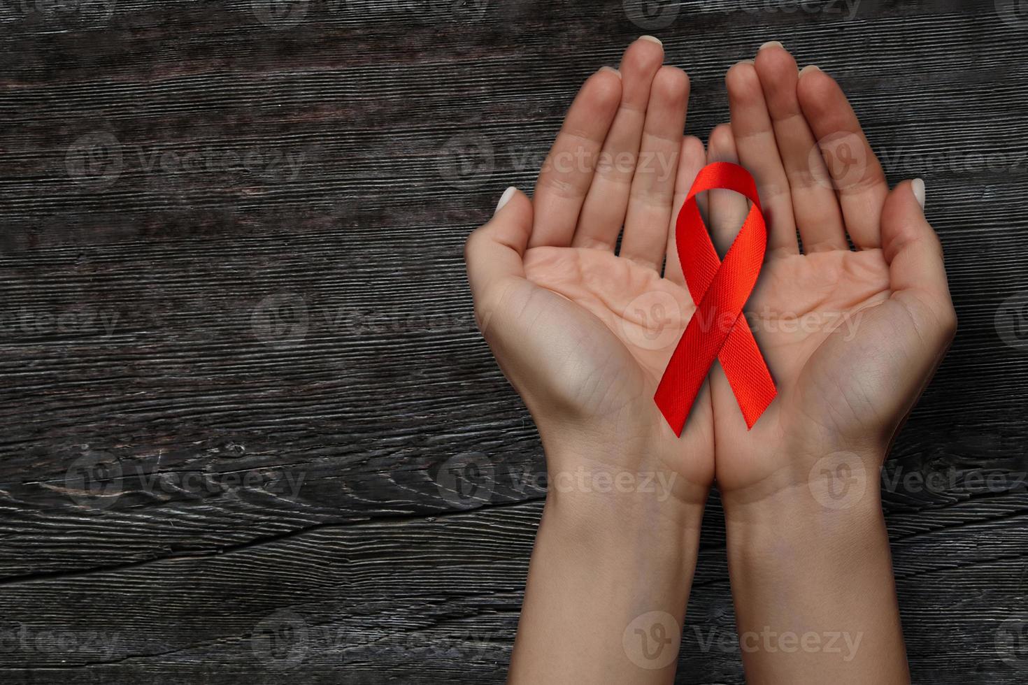 a red ribbon for the WORLD AIDS symbol is held on a wooden table photo