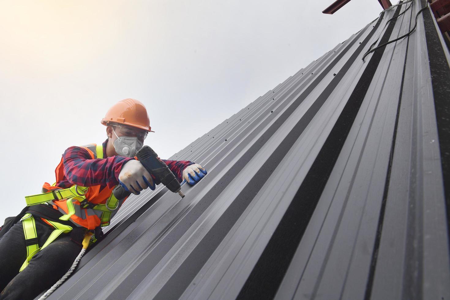 trabajador de techado con uniforme protector y guantes, herramientas para  techos, instalación de techos nuevos en construcción, taladro eléctrico  usado en techos nuevos con láminas de metal. 15632779 Foto de stock en