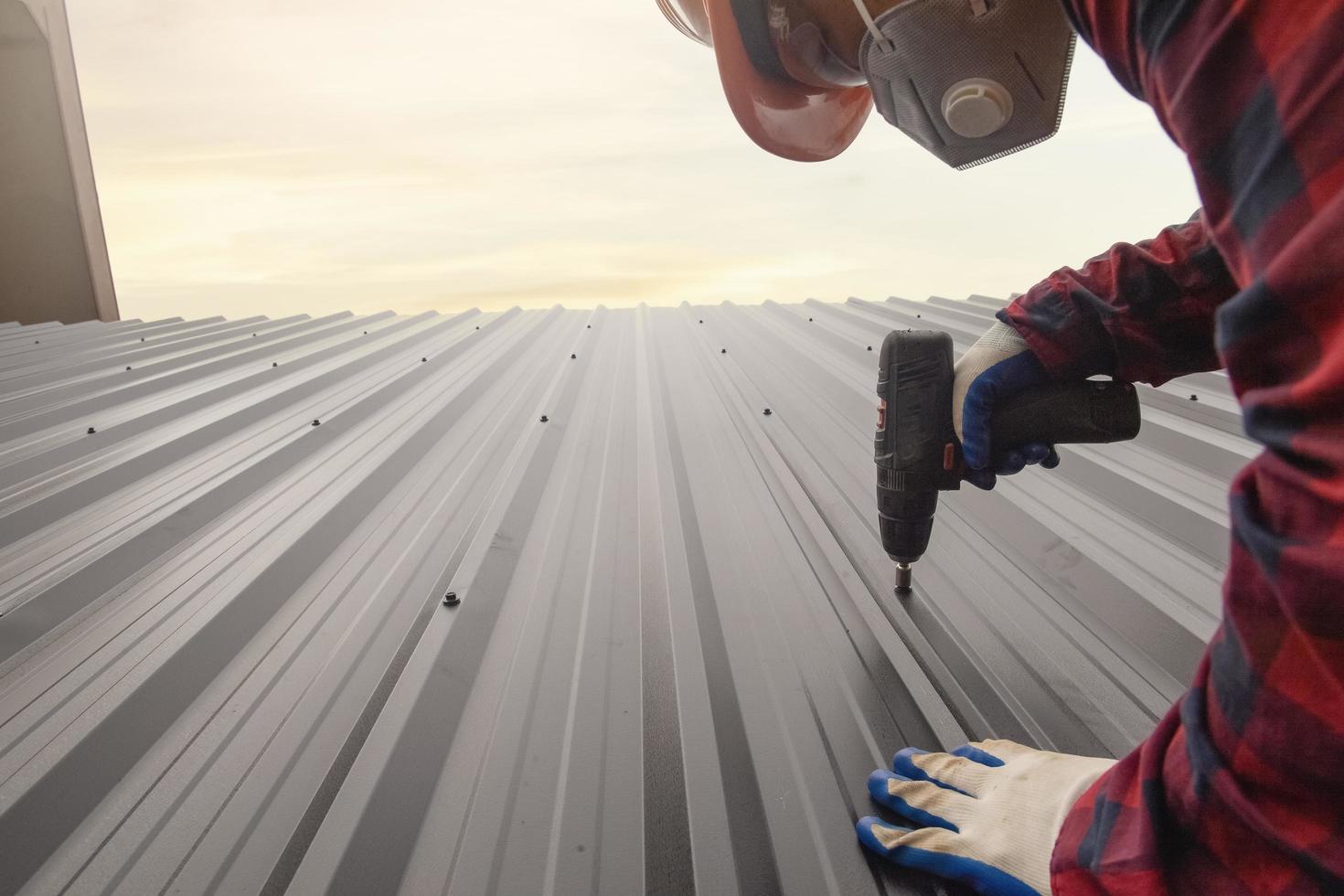close up drill Roofer worker  in protective uniform wear and gloves,Roofing tools,installing new roofs under construction,Electric drill used on new roofs with metal sheet. photo