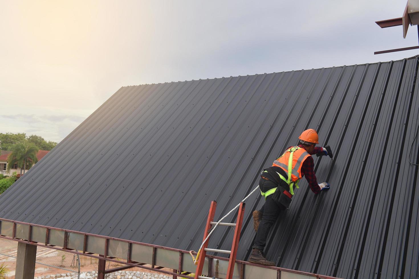 Roofer worker use the ladder in protective uniform wear and gloves,Roofing tools,installing new roofs under construction,Electric drill used on new roofs with metal sheet. photo