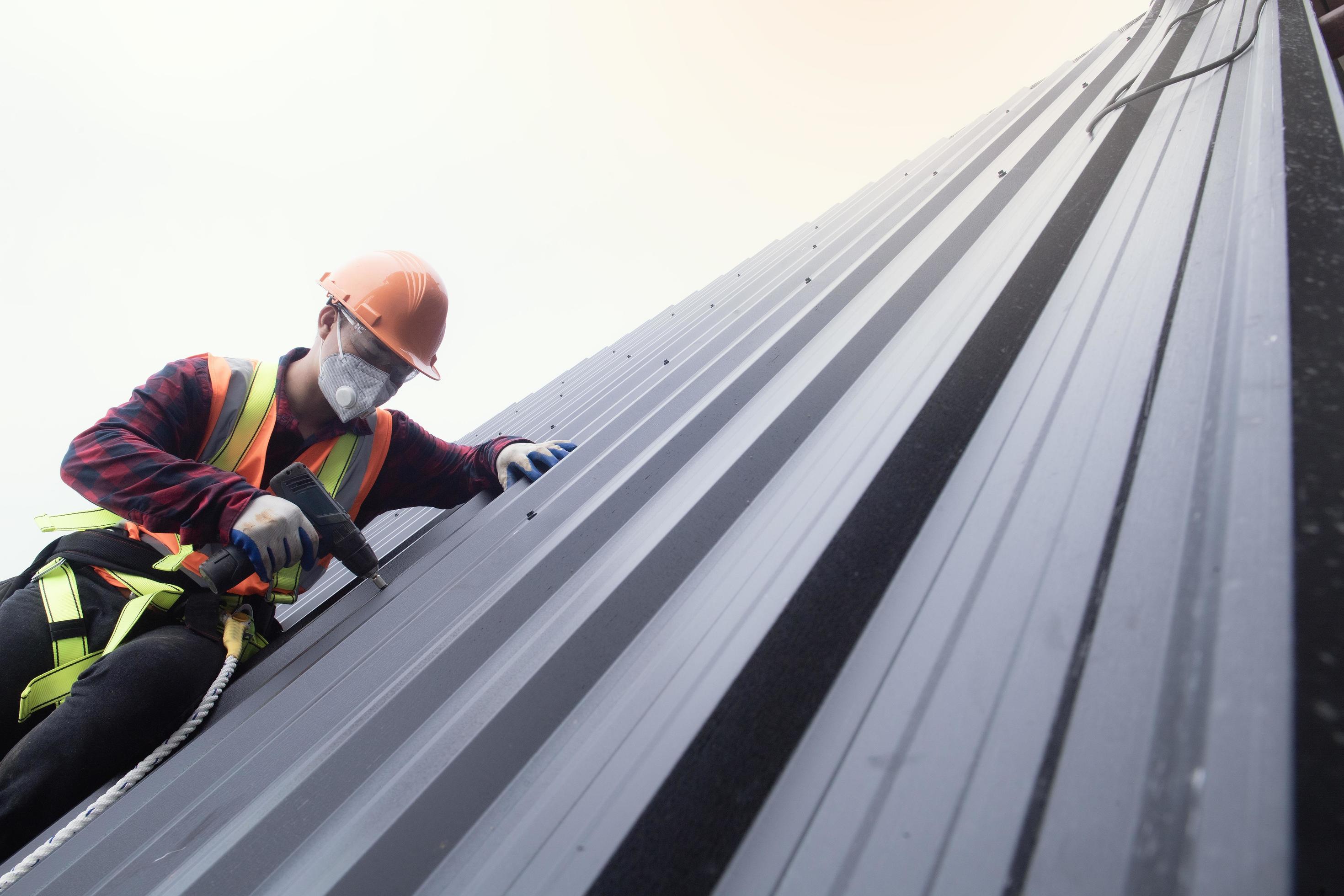 trabajador de techado con uniforme protector y guantes, herramientas para  techos, instalación de techos nuevos en construcción, taladro eléctrico  usado en techos nuevos con láminas de metal. 15632734 Foto de stock en