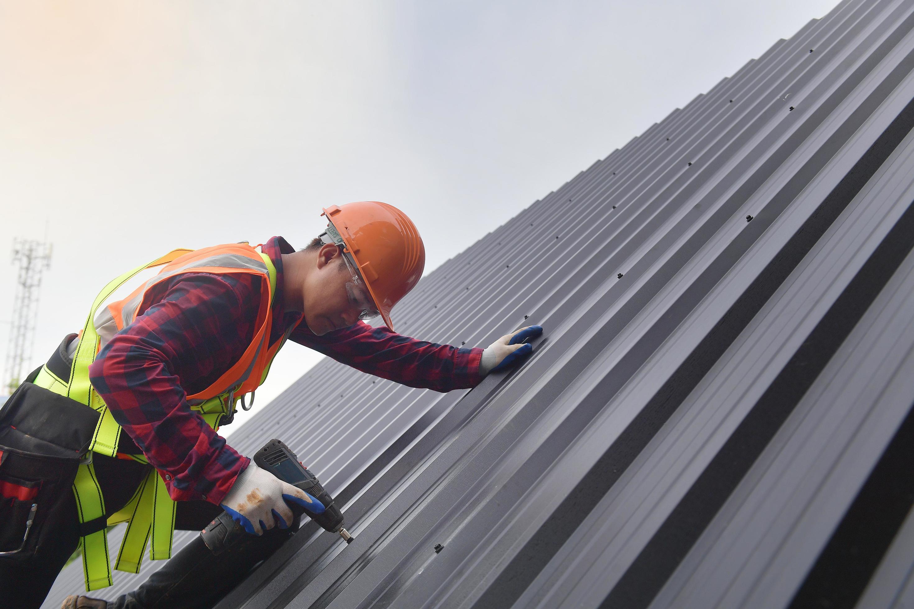 trabajador de techado con uniforme protector y guantes, herramientas para  techos, instalación de techos nuevos en construcción, taladro eléctrico  usado en techos nuevos con láminas de metal. 15632734 Foto de stock en